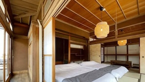 A traditional Japanese-style room with tatami flooring, a large bed with white bedding, sliding doors, and a hanging light fixture. - Hayase House (Kure)