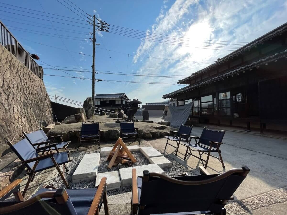 An outdoor seating area with chairs and a fire pit, surrounded by stone walls and traditional buildings.