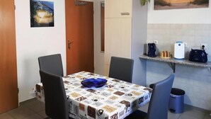 Un pequeño comedor con una mesa cubierta por un mantel estampado, dos sillas, un tazón azul y un mueble con puerta blanca.