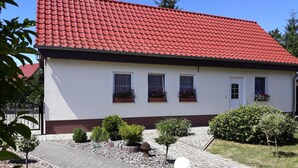Un edificio blanco con techo de tejas rojas, tres ventanas con jardineras y un camino pavimentado con árboles pequeños y una luz esférica.