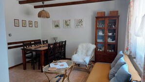 A dining area with a wooden table and chairs, a glass-top coffee table with a lace doily, a wicker chair with a fluffy cushion, a wooden cabinet with glass doors, and a sofa with a throw blanket. - Appartment, Wieliczka by Cracow (Wieliczka)