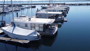 A marina with multiple boats docked, a covered boat, and a building with large windows. - Hausboot in Boltenhagen (Boltenhagen)