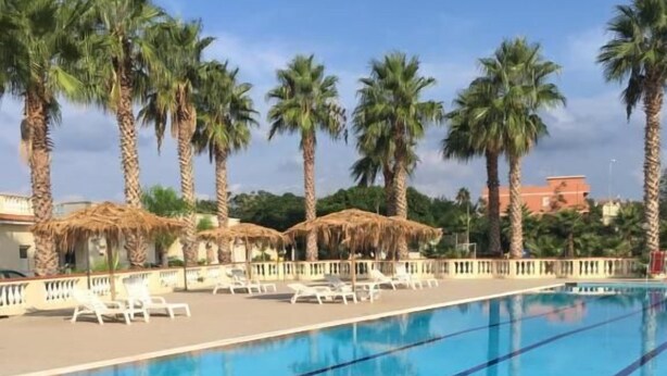 A swimming pool with clear blue water, surrounded by palm trees and lounge chairs. - Baia dello Stretto (Reggio Calabria)