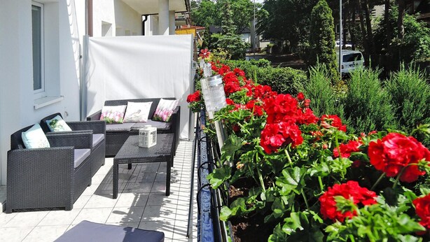 An outdoor seating area with wicker furniture and a garden bed with red flowers. - Terraced House Near Baltic Sea & Wolinski Park (Międzyzdroje)