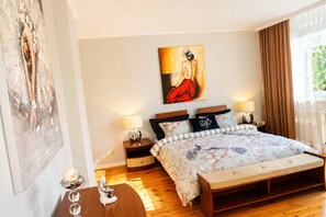 A bedroom with a large bed, two bedside tables, a nightstand, a painting on the wall, and a window with curtains. - Terraced House Near Baltic Sea & Wolinski Park (Międzyzdroje)