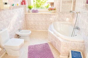 A bathroom with a bathtub, toilet, bidet, and a window with plants. - Terraced House Near Baltic Sea & Wolinski Park (Międzyzdroje)