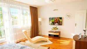 A bedroom with a bed, a TV, a clock, and a wooden floor. - Terraced House Near Baltic Sea & Wolinski Park (Międzyzdroje)