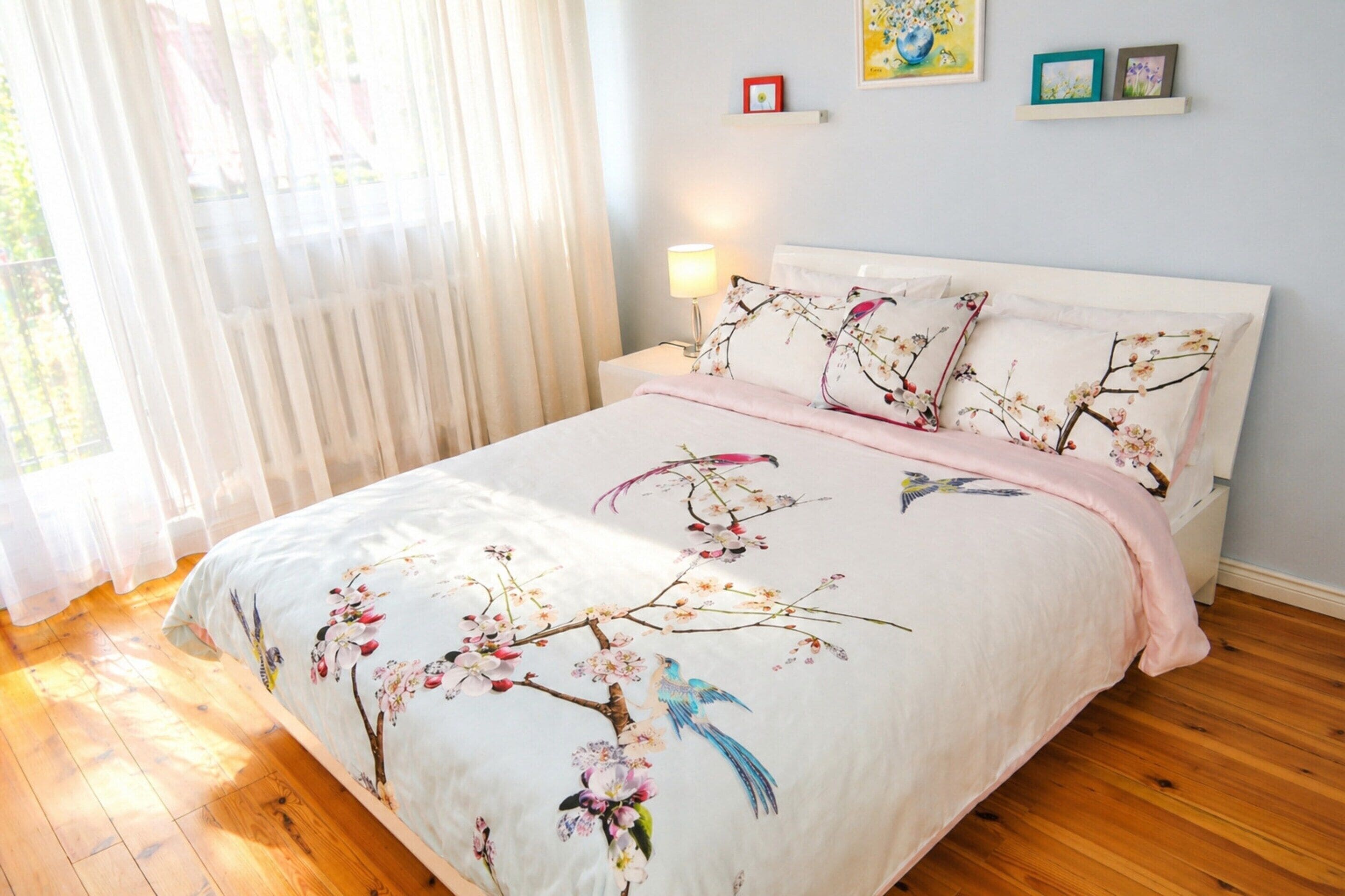 A bedroom with a bed, a nightstand, a lamp, and a window with sheer curtains.