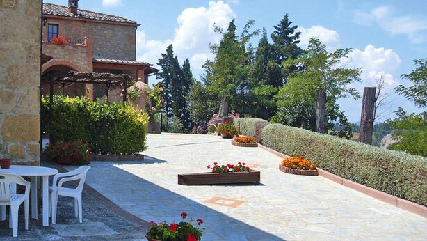 Un patio de piedra con mobiliario exterior, jardineras y un edificio con tejado de baldosas.