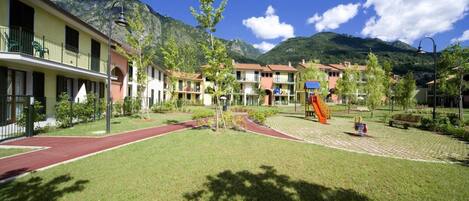 A hotel courtyard with a playground, a red running track, and mountain views.