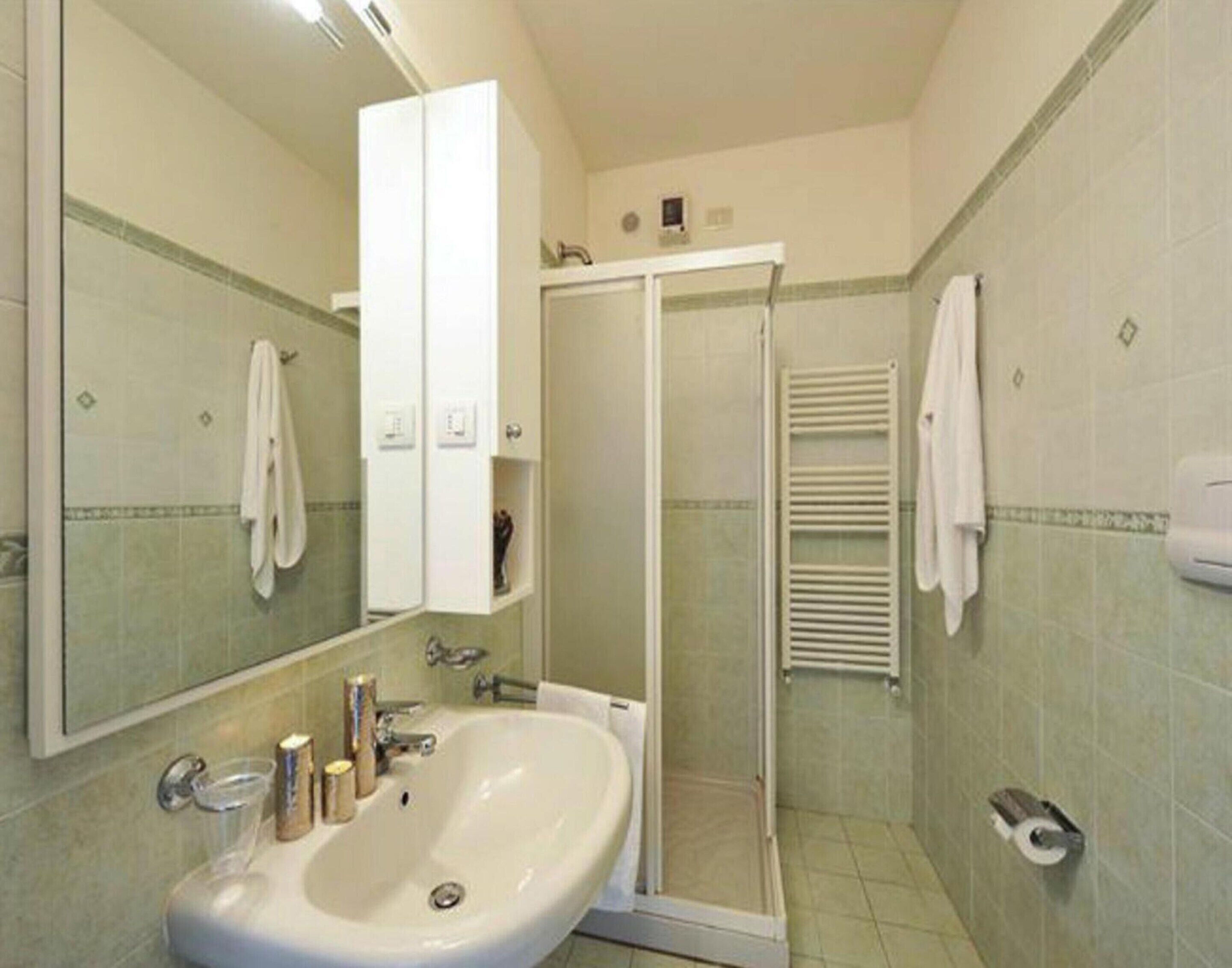A bathroom with a large sink, a mirror, a shower enclosure, and a towel rack.