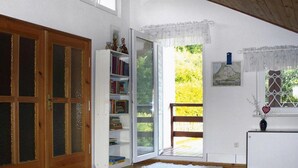 Een kamer met een houten deur, een witte boekenkast, een witte console en uitzicht door een glazen deur op een buitenruimte.