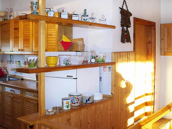 A kitchen with wooden cabinets, a refrigerator, and various kitchenware on shelves. - Beautiful Holiday Home in Zawory With Terrace (Chmielno)