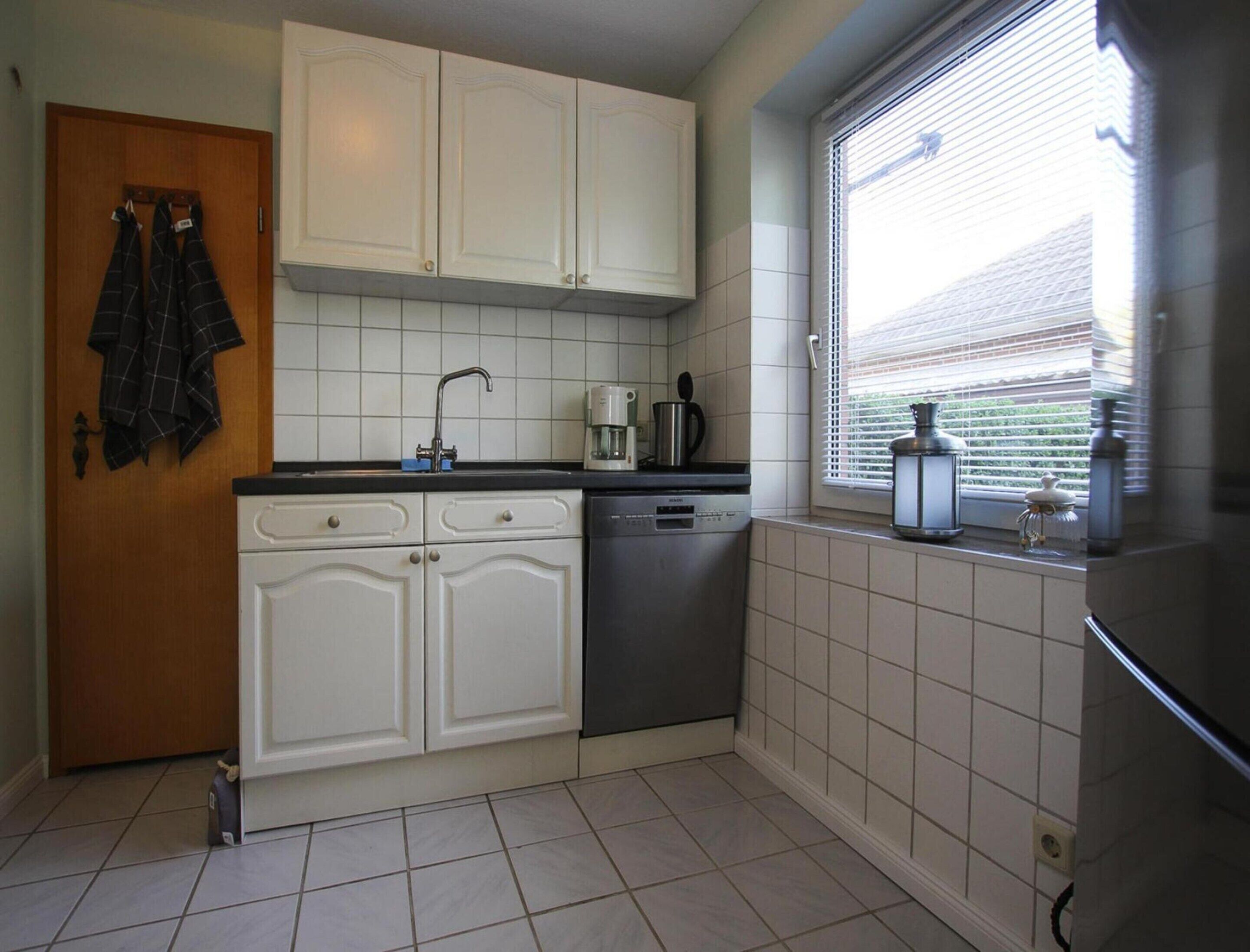 A kitchen with white cabinets, a dishwasher, and a window with blinds.