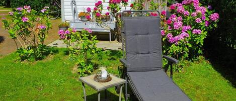 A garden with a lounge chair, a small table, and a shed in the background.