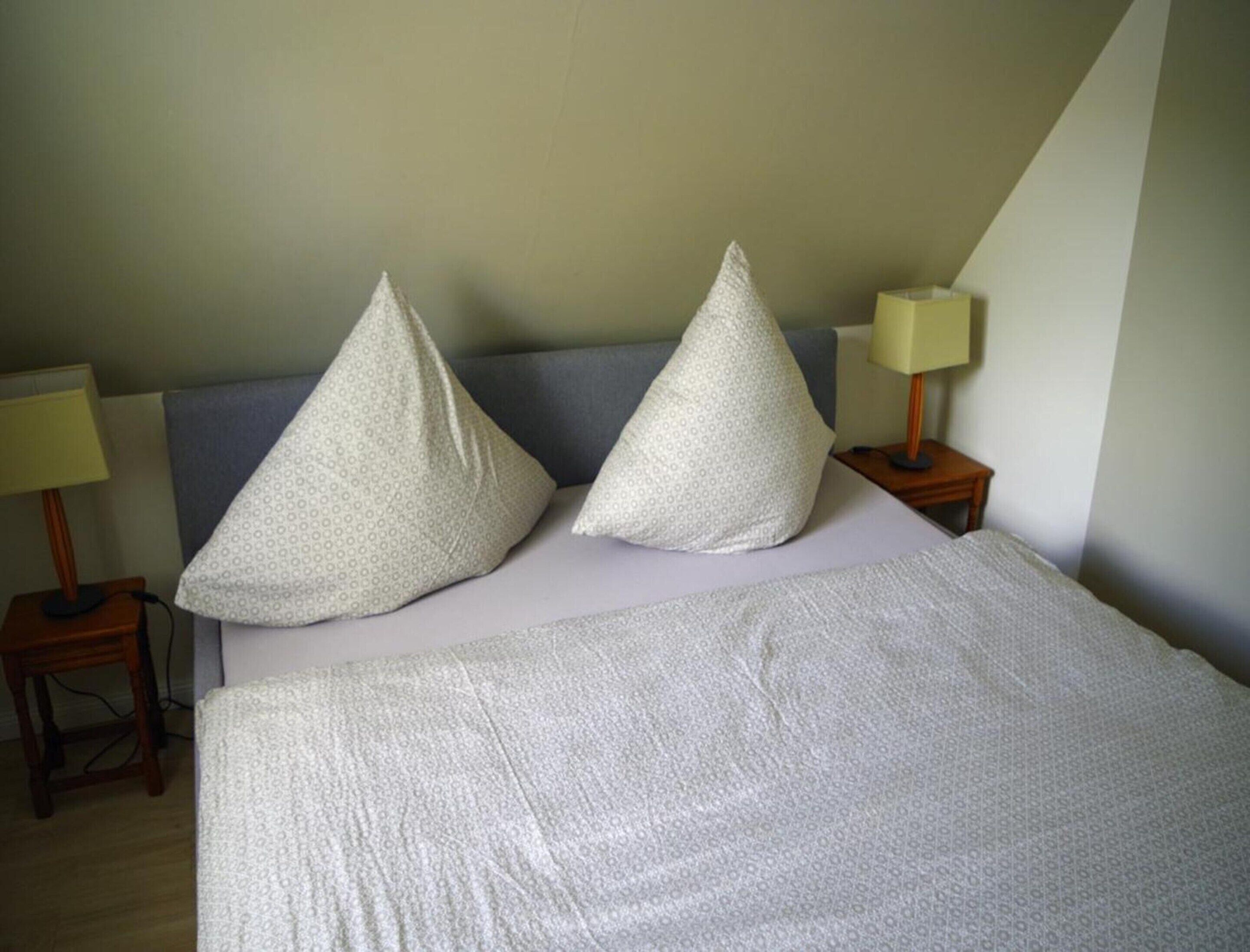 A neatly made bed with two pillows, a bedside table with a lamp, and a nightstand with a lamp.