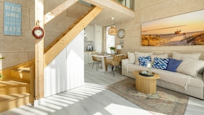 Interior moderno com escada, área de jantar e sala de estar com sofá e pintura de uma paisagem praiana.