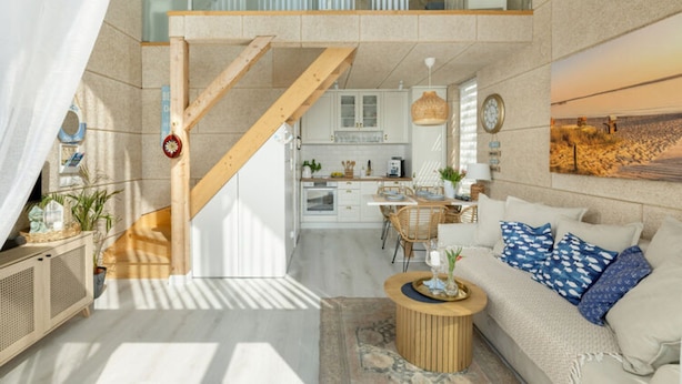 Uma sala de estar ampla com escada, cozinha ao fundo e um espaço de estar aconchegante com mesa de centro redonda.