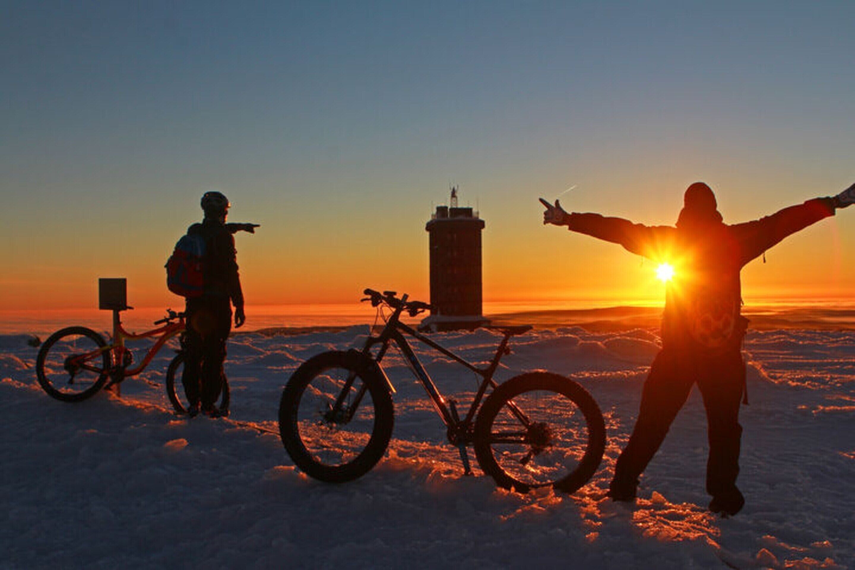 A person standing with arms outstretched in a snowy landscape at sunset.