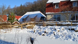 Paisaje nevado con una valla de madera, un edificio pequeño con techo rojo y una construcción más grande con techo blanco.