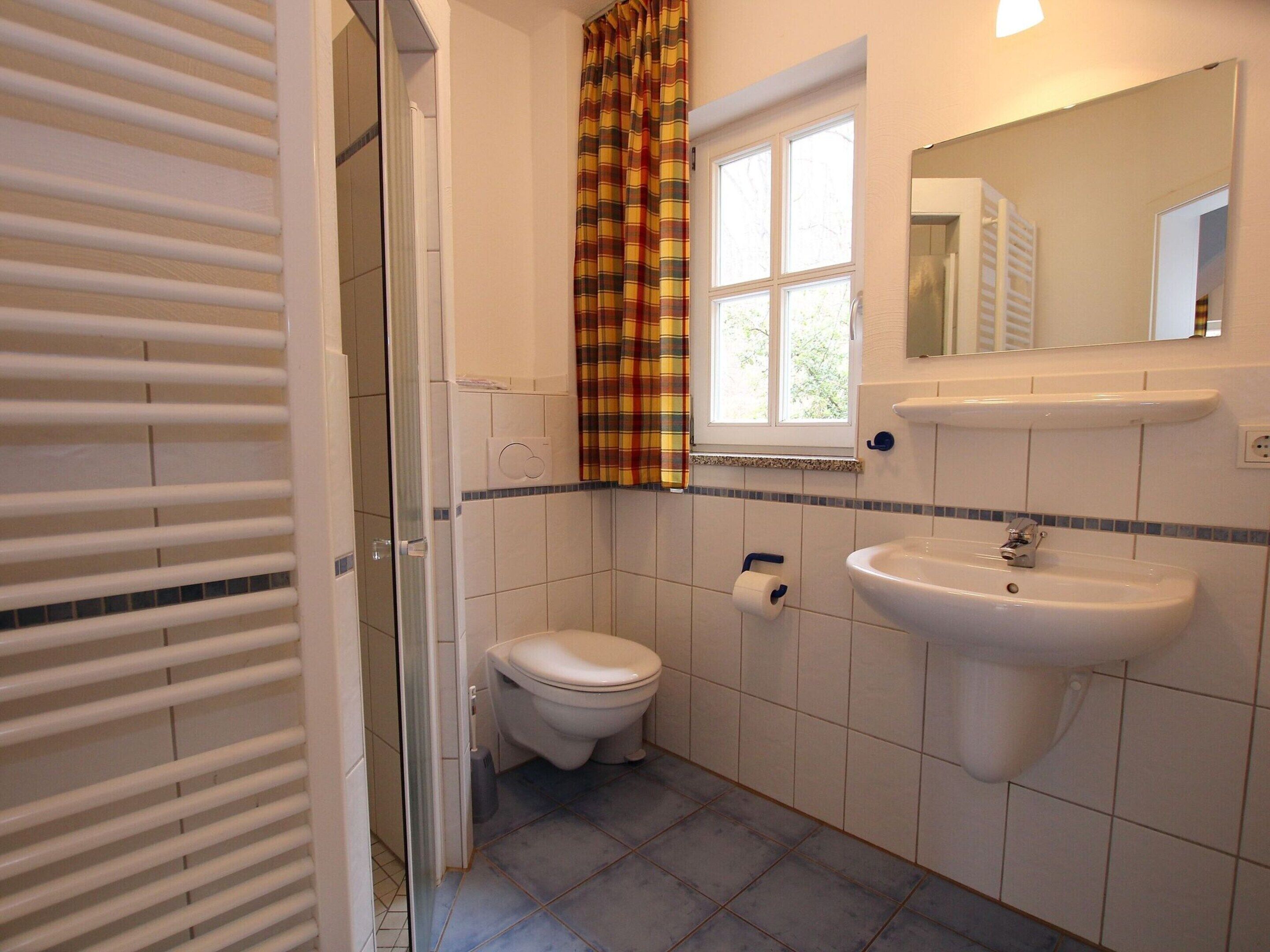 A small bathroom with a toilet, sink, and a window with a curtain.