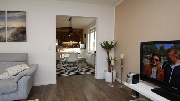 Un salon moderne avec un canapé gris, un téléviseur à écran plat et un coin repas comprenant une table et des chaises en bois.