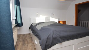 Une chambre moderne avec un lit blanc, un plancher en bois et une grande fenêtre avec des rideaux.