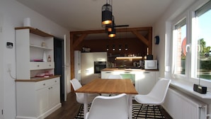 Une cuisine de taille réduite avec des meubles blancs, une table à manger en bois et des chaises blanches.