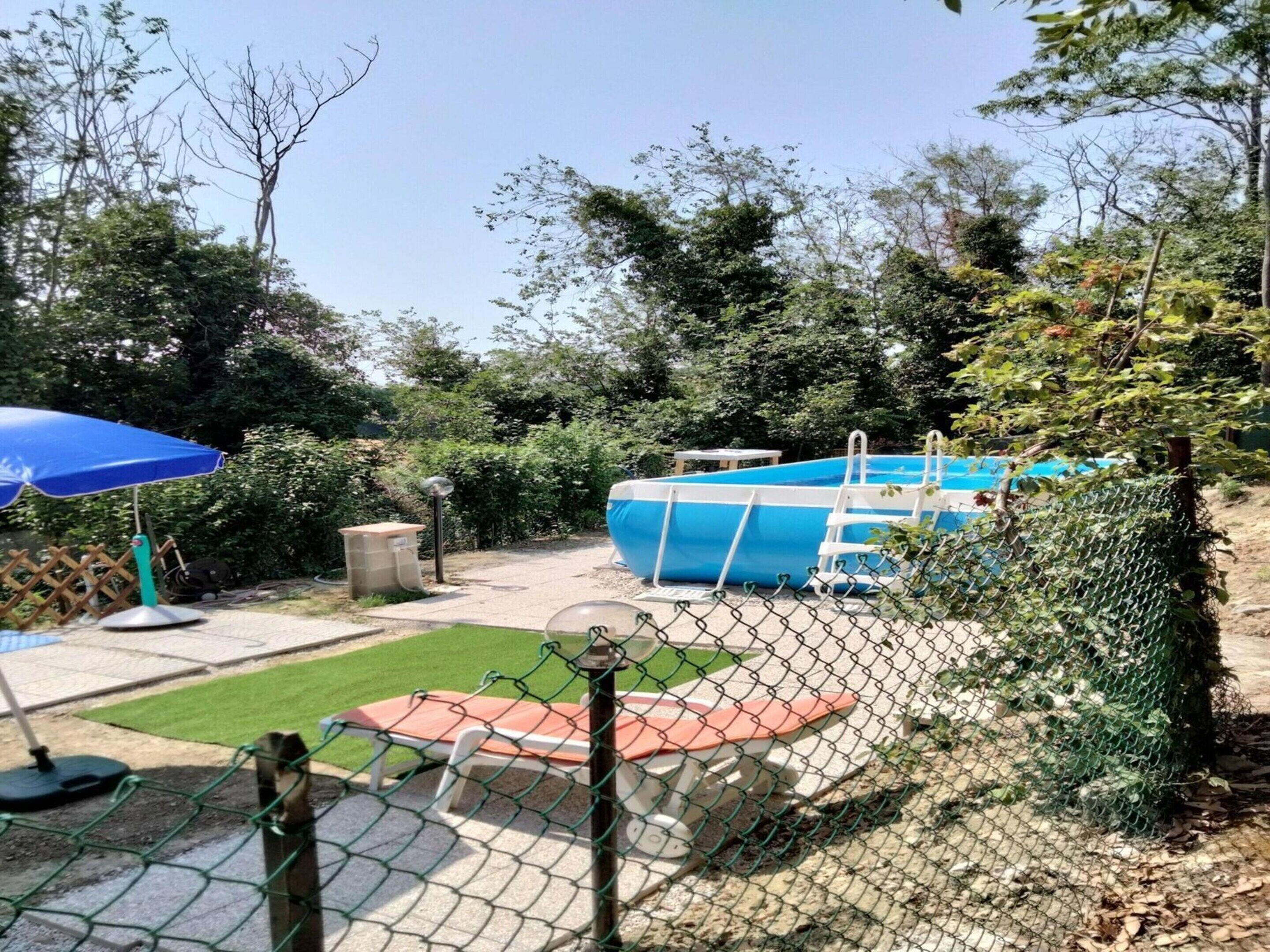 Un giardino sul retro con una piscina, un ombrellone blu, un tavolino e un prato verde.