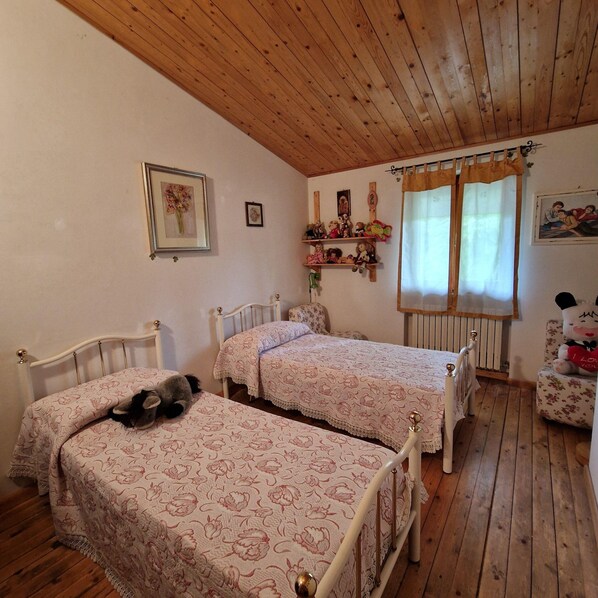 A room with two beds, wooden ceiling, and a window with curtains.