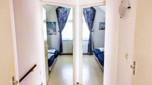 A corridor leading to two bedrooms with beds, a radiator, and a painting on the wall. - Bungalow in Breskens near Beach & Lighthouse (Breskens)