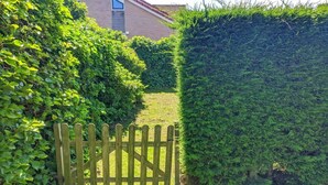 A wooden gate leading to a pathway flanked by dense green hedges. - Bungalow in Breskens near Beach & Lighthouse (Breskens)