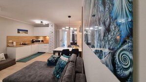 A modern living room with a grey sofa, a dining area with a table and chairs, a kitchen with white cabinets, and a large abstract painting on the wall. - Spacious Apartment in Mielno With Private Terrace (Mielno)