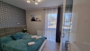 A modern bedroom with a large bed, a ceiling light fixture, a radiator, and a view of the outside through a glass door. - Spacious Apartment in Mielno With Private Terrace (Mielno)