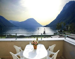 Una terraza con una mesa y sillas, con vista a un lago y montañas al fondo.