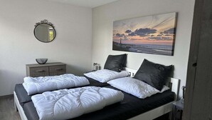 A bedroom with a bed, pillows, a bedside table, a mirror, a picture on the wall, and a small cabinet. - Bungalow in Breskens near Beach & Lighthouse (Breskens)