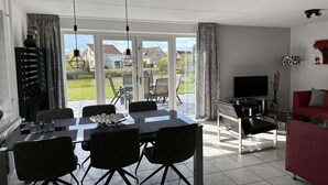 A modern living room with a dining area, a TV, and a red sofa. - Bungalow in Breskens near Beach & Lighthouse (Breskens)