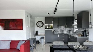 A compact living space with a kitchenette, a dining area, a red sofa, and a wall clock. - Bungalow in Breskens near Beach & Lighthouse (Breskens)