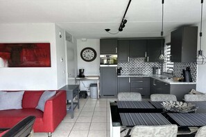 A compact living space with a kitchenette, a dining area, a red sofa, and a wall clock. - Bungalow in Breskens near Beach & Lighthouse (Breskens)