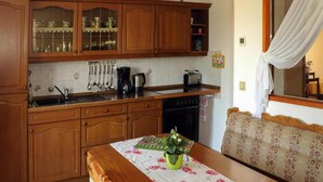A kitchen with wooden cabinets, a sink, a stove, and a dining table with a floral tablecloth. - Ferienwohnung Festungsblick in Pirna (Pirna)