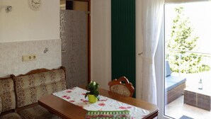 A room with a wooden table, floral-patterned sofa, a clock on the wall, and a view of greenery outside. - Ferienwohnung Festungsblick in Pirna (Pirna)