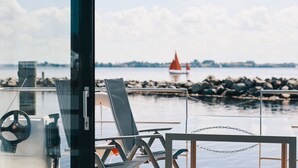 Uitzicht vanaf het dek van een boot, met een stuurwiel, een hekwerk en een afgelegen zeilboot.