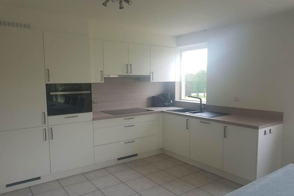 A kitchen with white cabinets, a built-in oven, a sink, and a window.