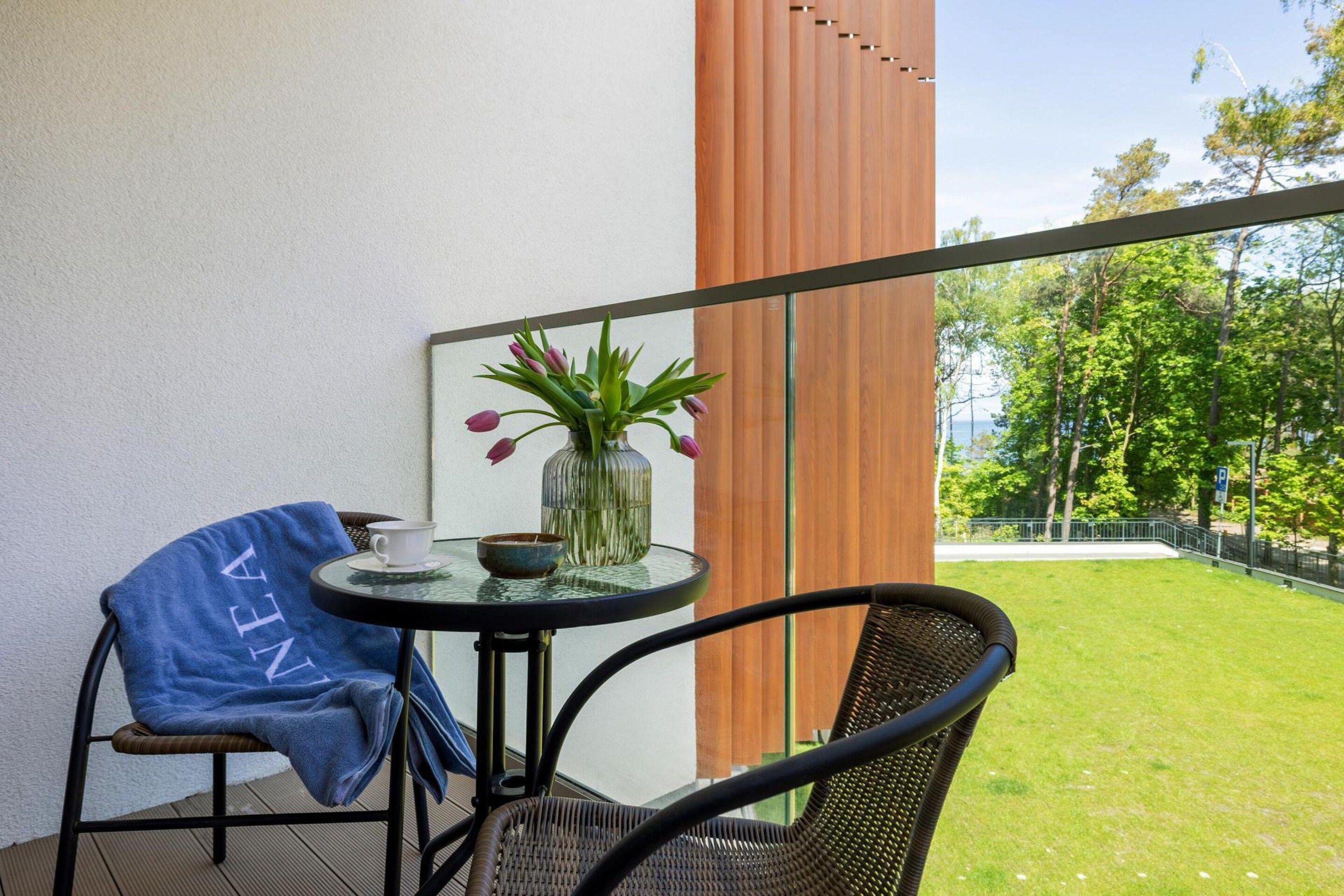 A balcony with a table, a chair, a vase with flowers, and a view of a green landscape.