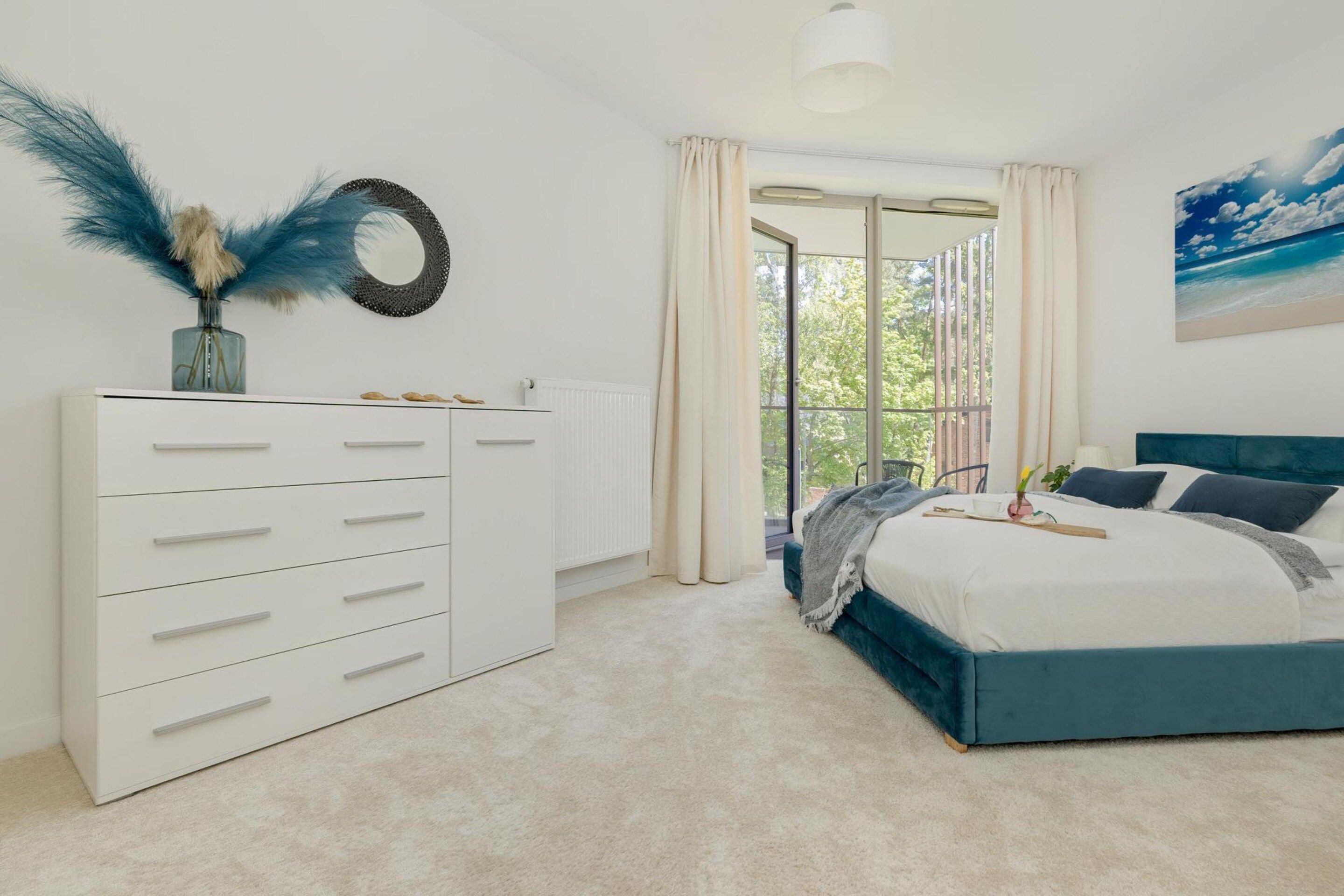 A bedroom with a bed, a dresser, a window with curtains, and a painting on the wall.