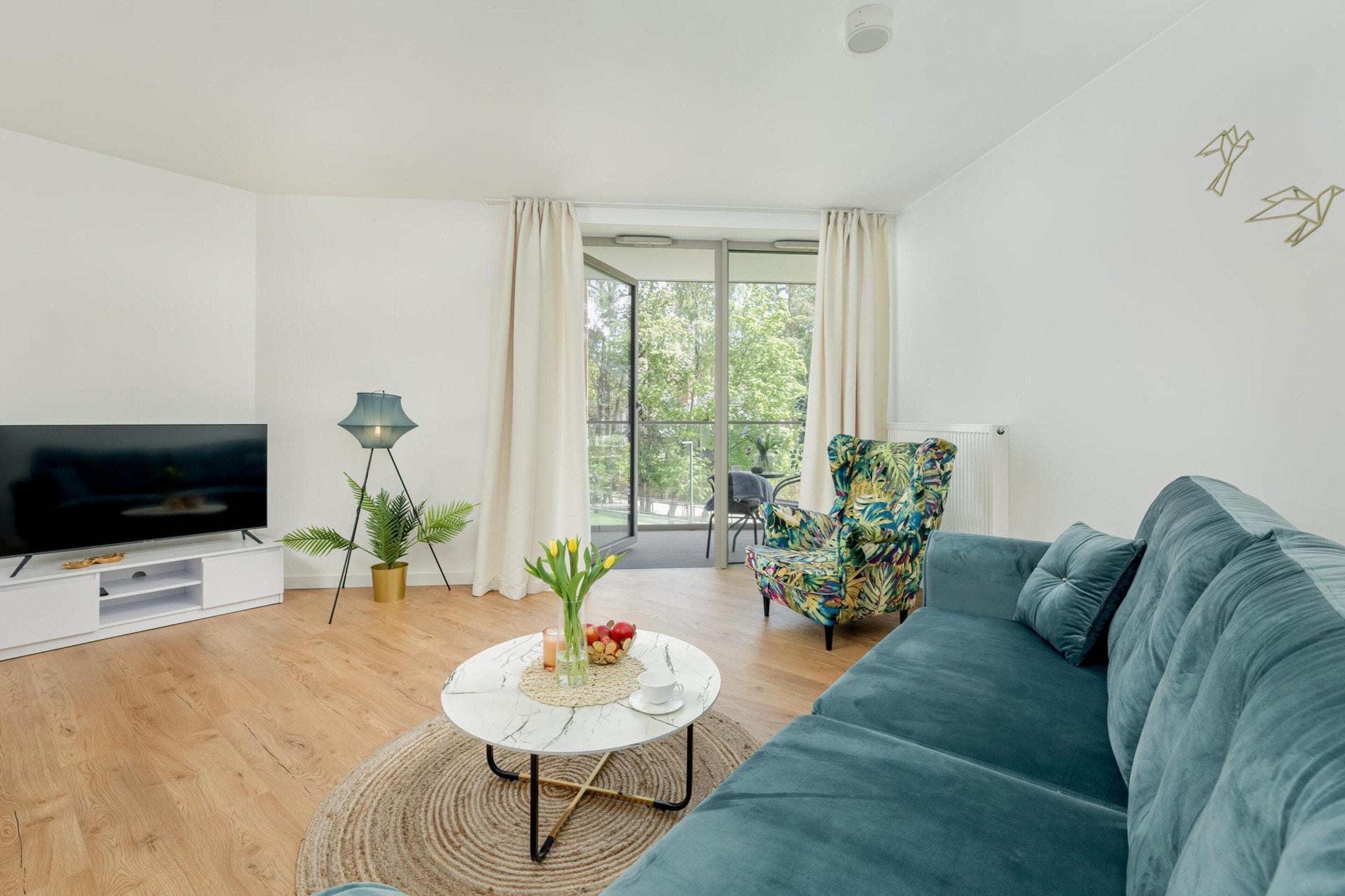 A modern living room with a flat-screen TV, a sofa, a colorful armchair, and a dining area with a table and chairs.