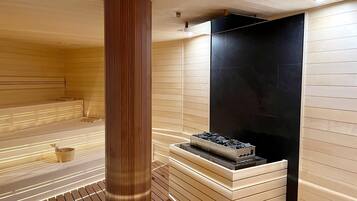 A sauna with wooden paneling, a central pillar, and a black stone wall.