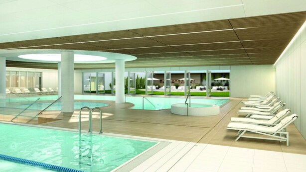 En moderne indendørs swimmingpool med flere baner, liggestole og et solterrasseområde.