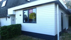 A white building with a black roof, a window with a sign, and a small hedge in front. - Family & Pet-Friendly Escape (Breskens)