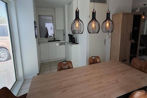 Zona pranzo con tavolo e sedie in legno, cucina sullo sfondo e tre lampade a sospensione.